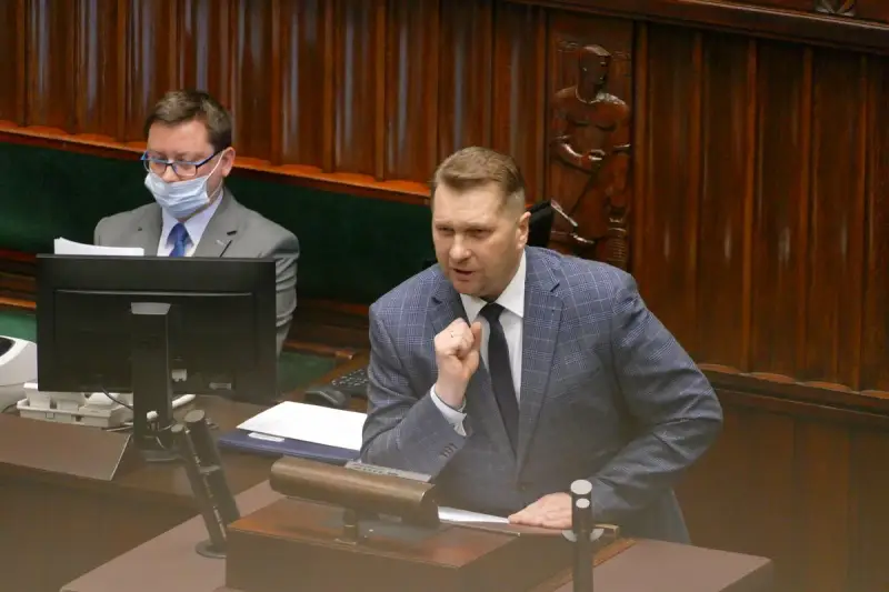 Poseł przemawia, dyskutując o tym, lex czarnek co zmienia. W tle siedzi inny poseł w masce.